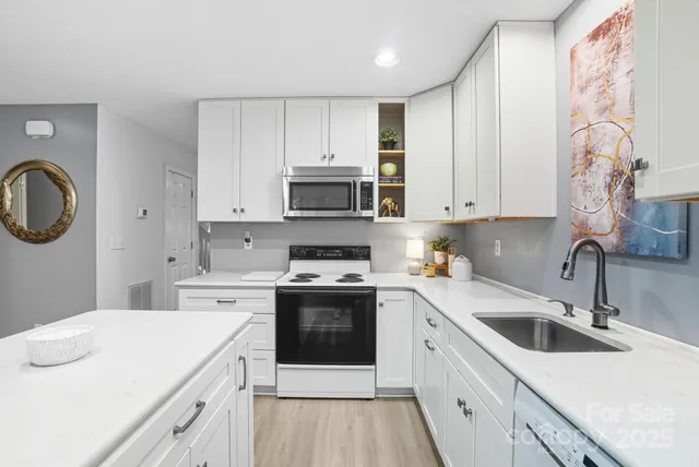 a kitchen with a sink dishwasher a stove top oven a refrigerator with white cabinets and wooden floor