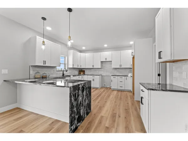 a kitchen with stainless steel appliances granite countertop a sink dishwasher a stove and white cabinets with wooden floor