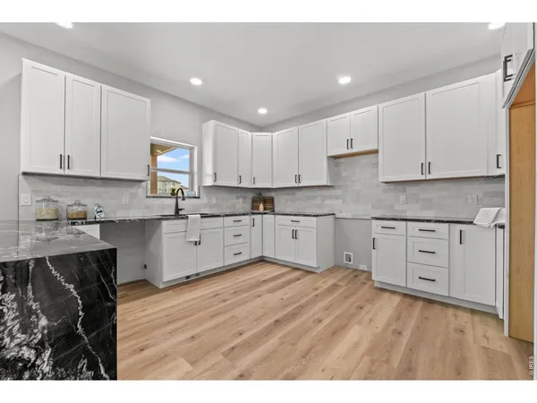 a large kitchen with cabinets stainless steel appliances granite countertop a stove a sink dishwasher and white cabinets with wooden floor