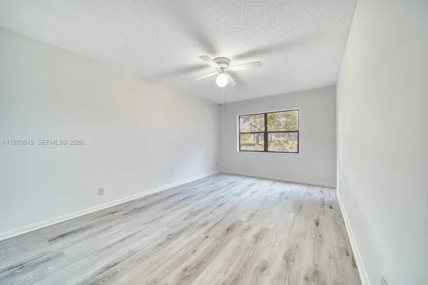 an empty room with wooden floor chandelier fan and windows