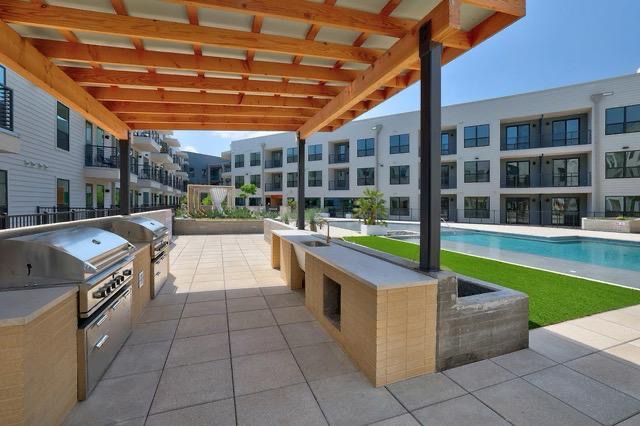 1701 Simond Avenue, Unit 615 Austin, TX 78723 - Photo 2 of 25 Outdoor grilling station featuring two built-in stainless steel grills, a light wood pergola, tiled countertops, and a full-size pool with surrounding artificial turf