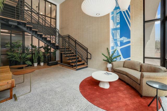1701 Simond Avenue, Unit 615 Austin, TX 78723 - Photo 21 of 25 Two-story entry foyer featuring a modern industrial staircase with wood treads and black metal railings, terrazzo-finish flooring, a textured light-toned brick accent wall, and expansive multi-pane windows