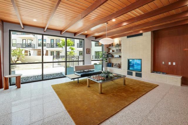 1701 Simond Avenue, Unit 615 Austin, TX 78723 - Photo 22 of 25 Wood-paneled ceiling with exposed beams, full-height window wall, built-in tiled fireplace with integrated shelving, and light-colored terrazzo flooring