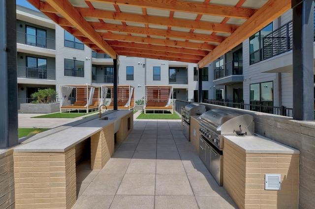 1701 Simond Avenue, Unit 615 Austin, TX 78723 - Photo 24 of 25 Outdoor grilling station featuring multiple built-in stainless steel grills, a sink, and expansive counter space under a slatted wood pergola