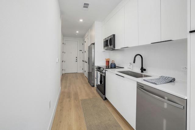 1701 Simond Avenue, Unit 615 Austin, TX 78723 - Photo 4 of 25 Contemporary kitchen featuring white flat-panel cabinetry, stainless steel appliances, a matte black gooseneck faucet, light-toned wood-finish flooring, and recessed lighting