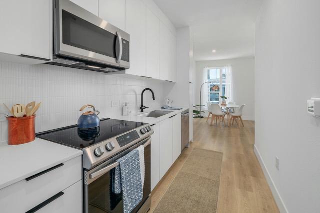 1701 Simond Avenue, Unit 615 Austin, TX 78723 - Photo 5 of 25 Kitchen featuring white cabinetry with matte black pulls, stainless steel appliances including an over-the-range microwave and electric range, white countertop space, and a white tiled backsplash