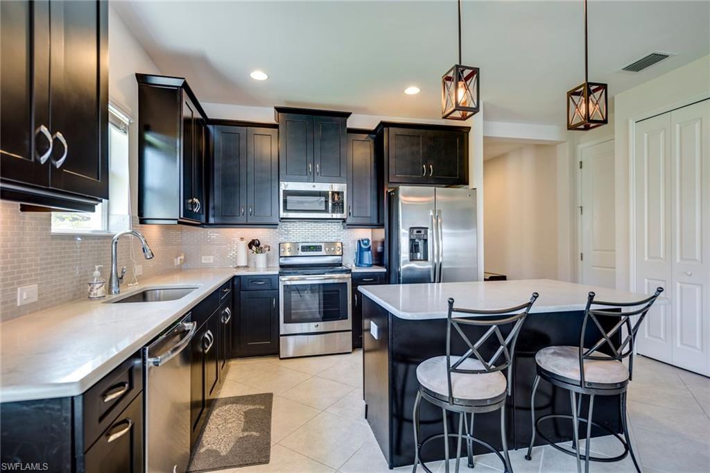 3782 Canopy Circle Naples, FL 34120 - Photo 16 of 31 a kitchen with stainless steel appliances a sink a stove a refrigerator cabinets a dining table and chairs