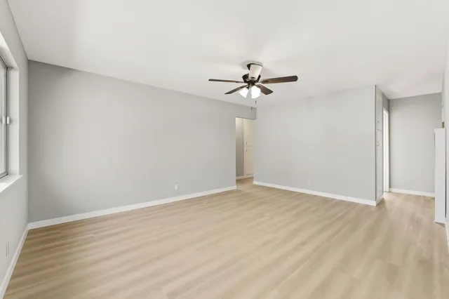 a view of an empty room with wooden floor and a ceiling fan