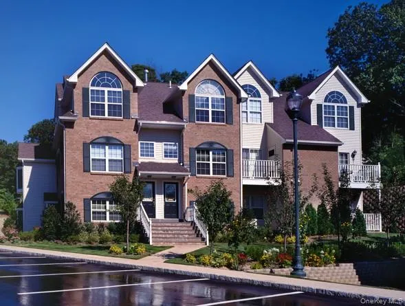 a view of a brick house with a yard plants and large tree