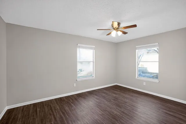 an empty room with wooden floor ceiling fan and windows