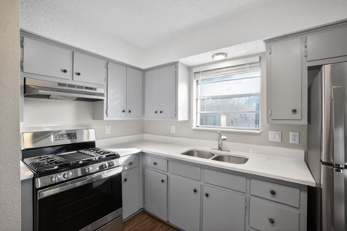 1505 Timber Street Georgetown, TX 78626 - Photo 9 of 22 Kitchen with stainless steel appliances, gray cabinets, under cabinet range hood, a textured ceiling, and dark wood finished floors