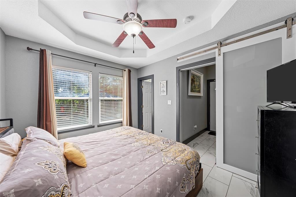 1205 North 17th Street Waco, TX 76707 - Photo 20 of 38 Bedroom featuring a barn door, a raised ceiling, light marble finish flooring, and ceiling fan