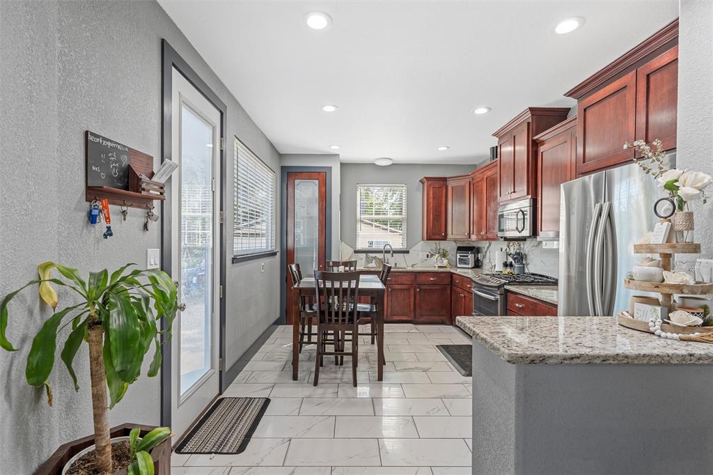 1205 North 17th Street Waco, TX 76707 - Photo 9 of 38 Kitchen with dark brown cabinets, decorative backsplash, appliances with stainless steel finishes, light stone counters, and a textured wall