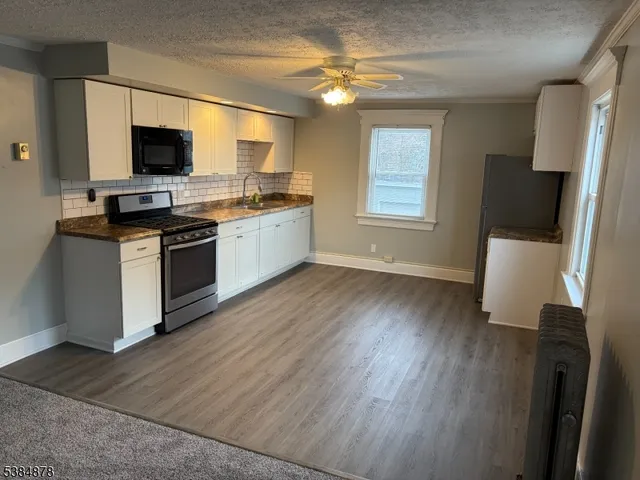 a kitchen with stainless steel appliances a stove a refrigerator a sink and white cabinets with wooden floor