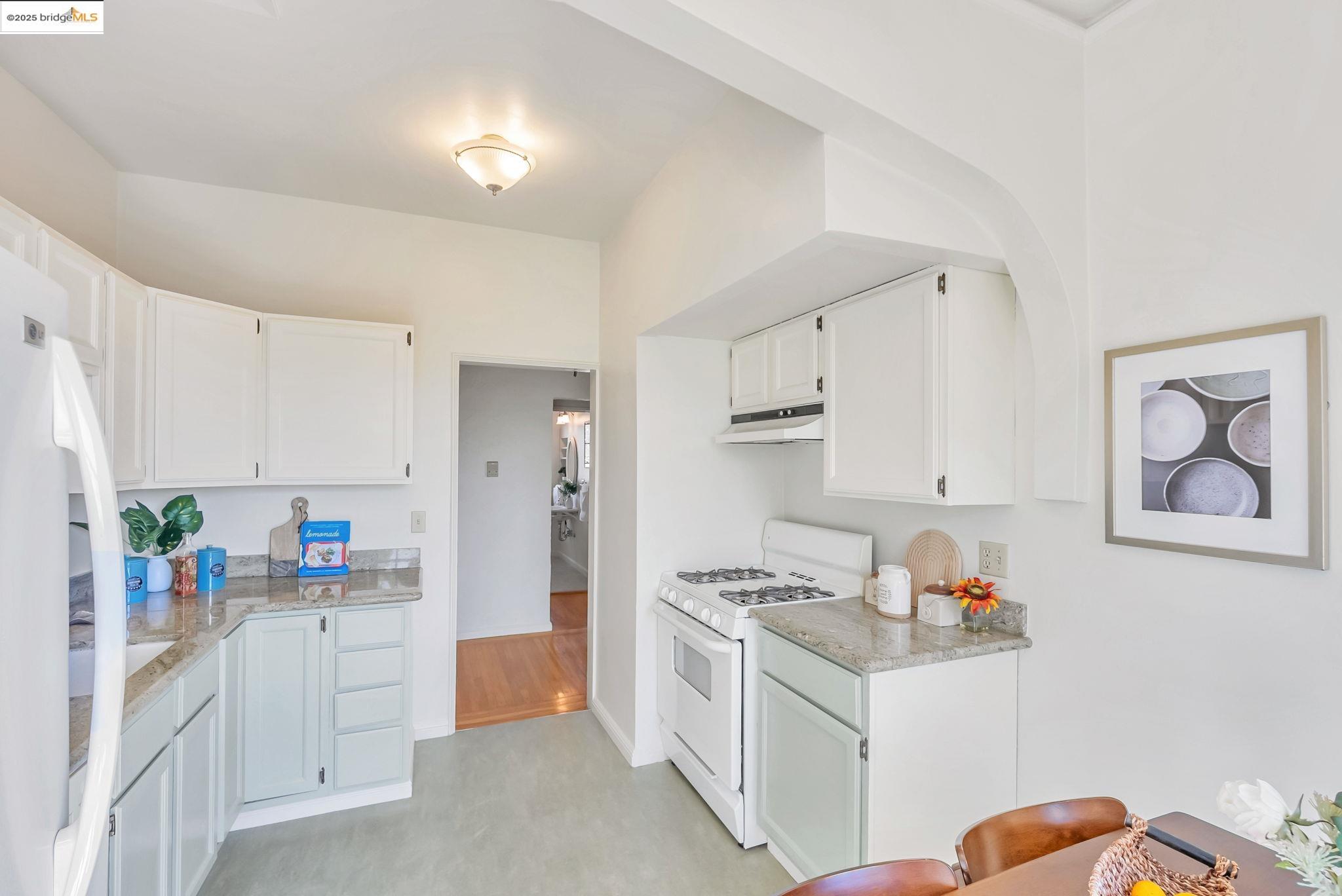 848 Stannage Avenue, Unit 11 Albany, CA 94706 - Photo 14 of 24 Kitchen with white appliances, white cabinets, under cabinet range hood, and light stone counters