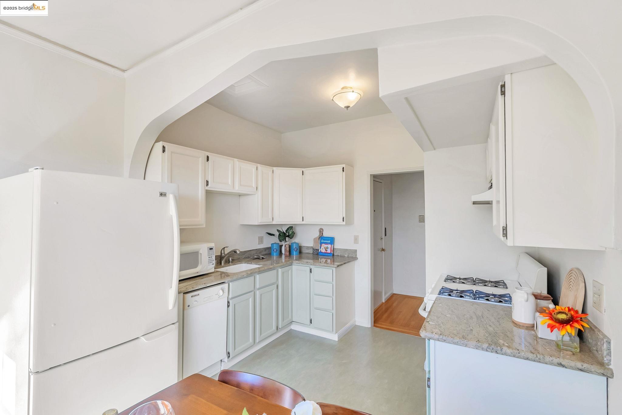 848 Stannage Avenue, Unit 11 Albany, CA 94706 - Photo 15 of 24 Kitchen with white appliances, white cabinetry, light stone countertops, and arched walkways