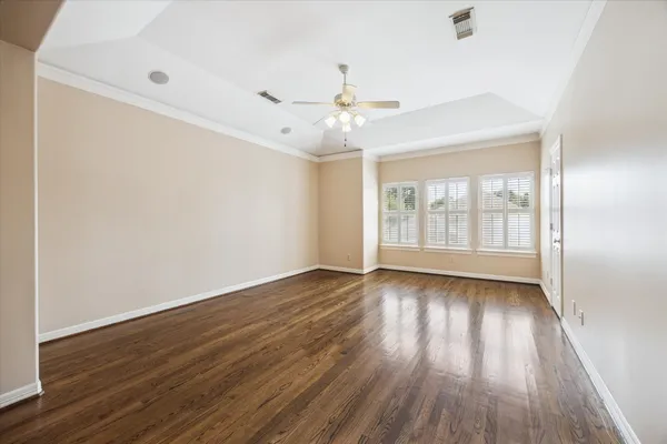 an empty room with wooden floor chandelier fan and windows