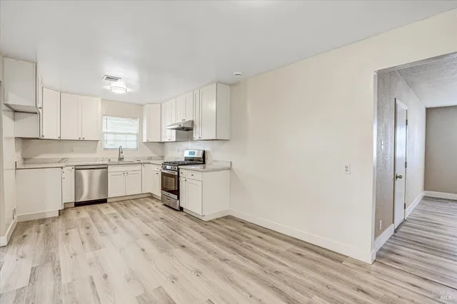 a kitchen with wooden floors white cabinets and stainless steel appliances