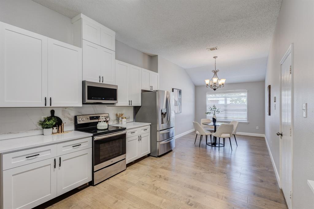7218 Compass Point Drive Rowlett, TX 75089 - Photo 17 of 30 Kitchen featuring appliances with stainless steel finishes, white cabinets, light wood-type flooring, a chandelier, and lofted ceiling