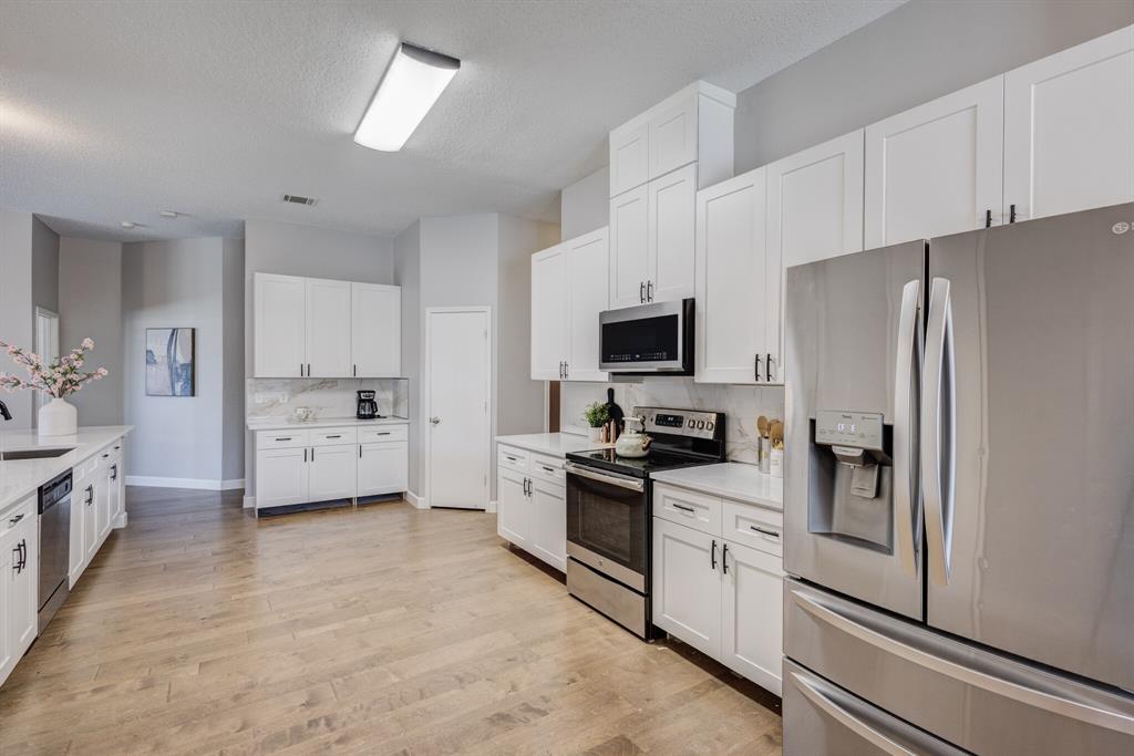 7218 Compass Point Drive Rowlett, TX 75089 - Photo 21 of 30 Kitchen with stainless steel appliances, decorative backsplash, white cabinetry, light wood-type flooring, and a textured ceiling