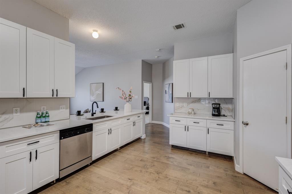 7218 Compass Point Drive Rowlett, TX 75089 - Photo 27 of 30 Kitchen featuring white cabinets, stainless steel dishwasher, backsplash, light wood-type flooring, and a textured ceiling