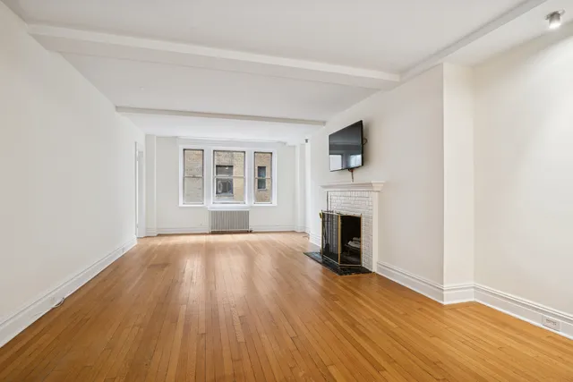 a view of an empty room with wooden floor fireplace and a window