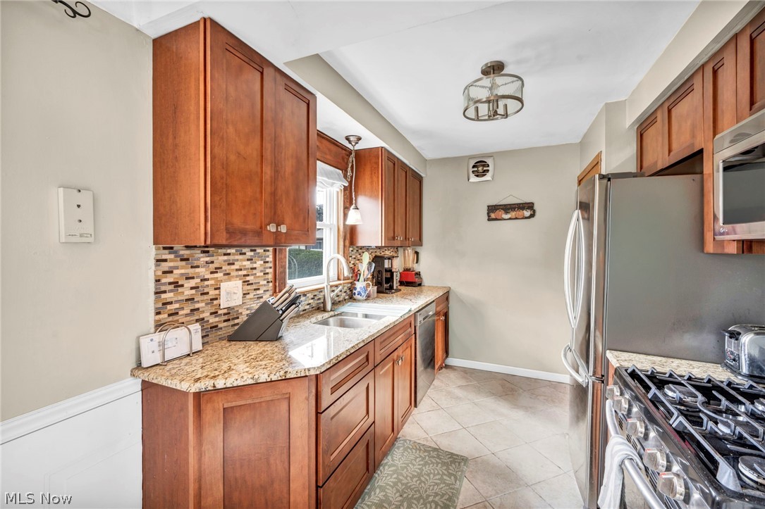 30002 Barjode Road Willowick, OH 44095 - Photo 16 of 33 Kitchen with light stone counters, stainless steel appliances, wood finish cabinets, backsplash, and light tile patterned flooring