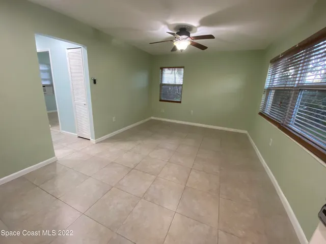 an empty room with chandelier fan and windows