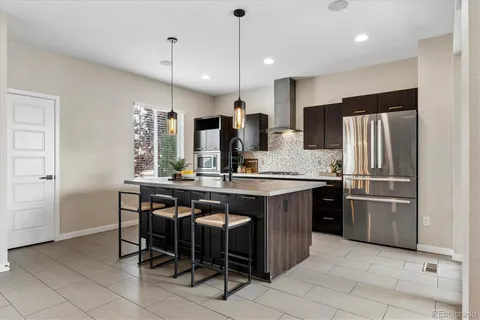 a kitchen with stainless steel appliances a sink a stove a refrigerator and chairs