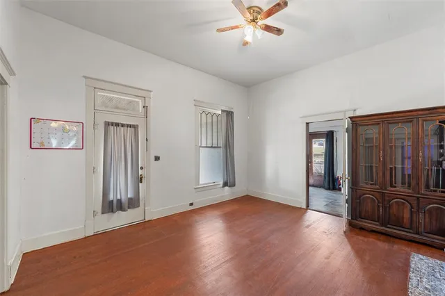 a view of an empty room with wooden floor and a ceiling fan