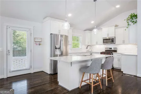 a kitchen with stainless steel appliances granite countertop a refrigerator a sink dishwasher a stove and white cabinets with wooden floor