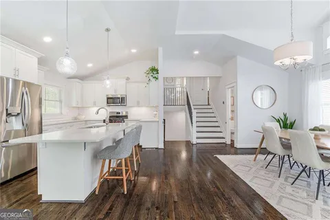 a kitchen with stainless steel appliances kitchen island granite countertop a refrigerator a stove a sink dishwasher and white cabinets with wooden floor