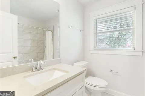 a bathroom with a granite countertop sink toilet a large mirror and a window
