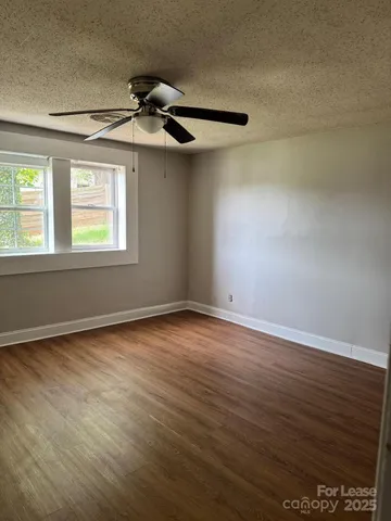 an empty room with wooden floor fan and windows