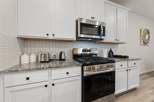 a kitchen with granite countertop white cabinets and stainless steel appliances