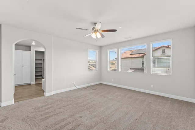 an empty room with chandelier fan and windows