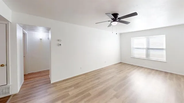 an empty room with wooden floor a ceiling fan and windows