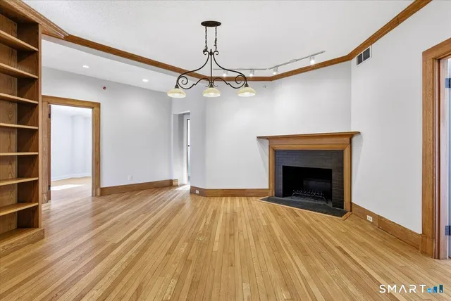 a view of an empty room with wooden floor fireplace and a window