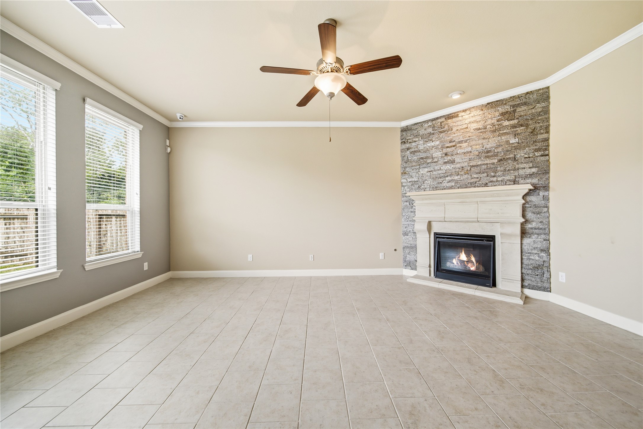 5303 Mesquite Willow Lane Rosharon, TX 77583 - Photo 5 of 32 Bright living room with tall ceilings, large windows, tile flooring, and a cozy fireplace that features a wall of accent stone. Neutral tones and a ceiling fan add comfort and style.