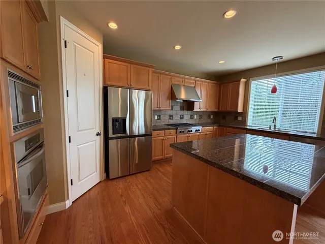 a kitchen with stainless steel appliances granite countertop a refrigerator a stove and a sink with wooden floors