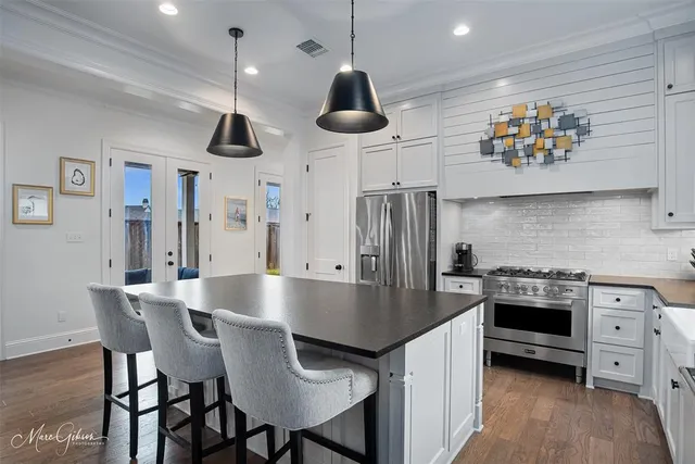 a kitchen with stainless steel appliances granite countertop a stove a refrigerator a kitchen island a dining table and chairs with wooden floor