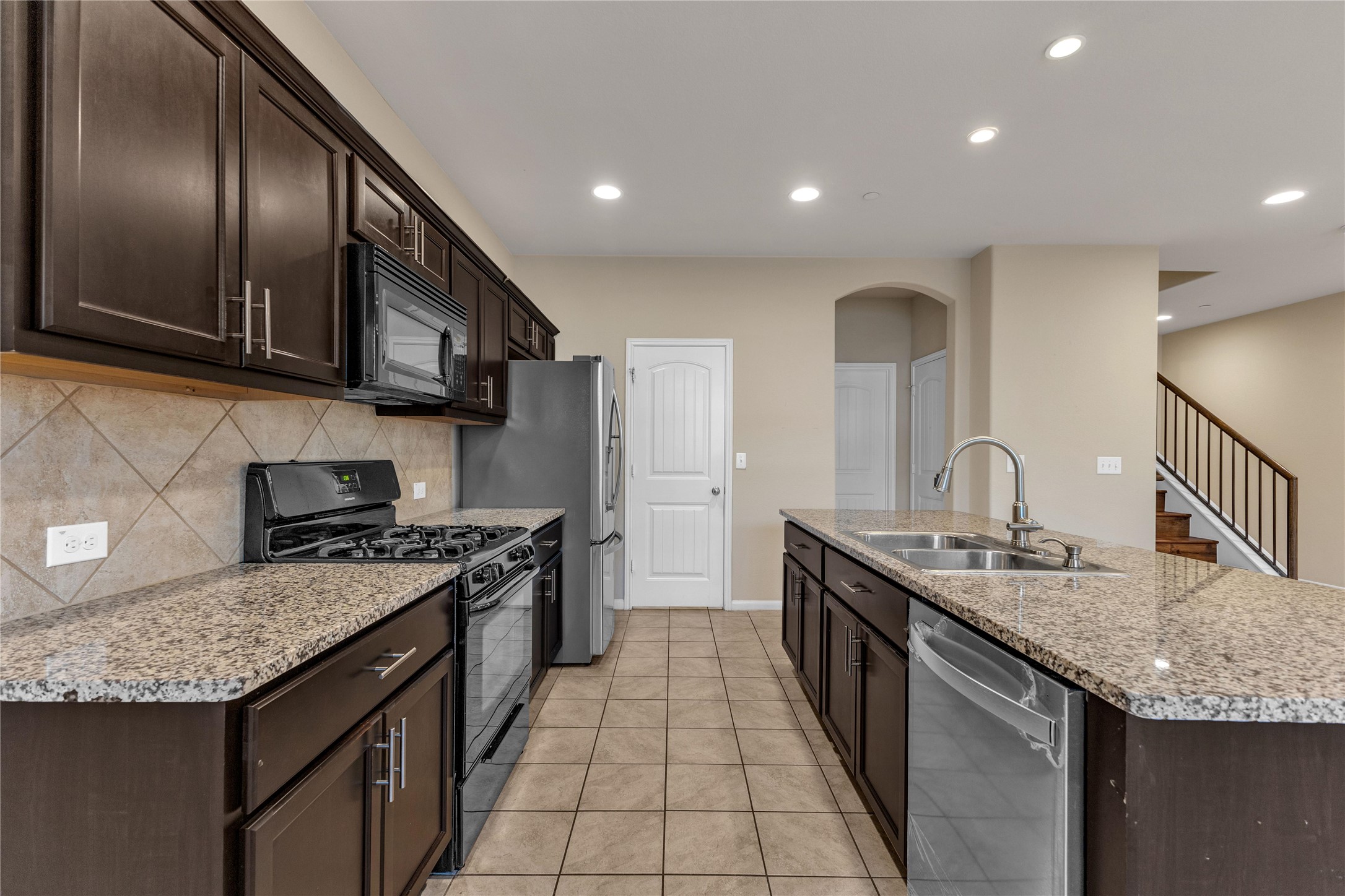 2880 Donnell Drive, Unit 2003 Round Rock, TX 78664 - Photo 12 of 31 Kitchen featuring dark wood-finish cabinetry, light speckled countertops, stainless steel appliances, a tile backsplash, and tile flooring