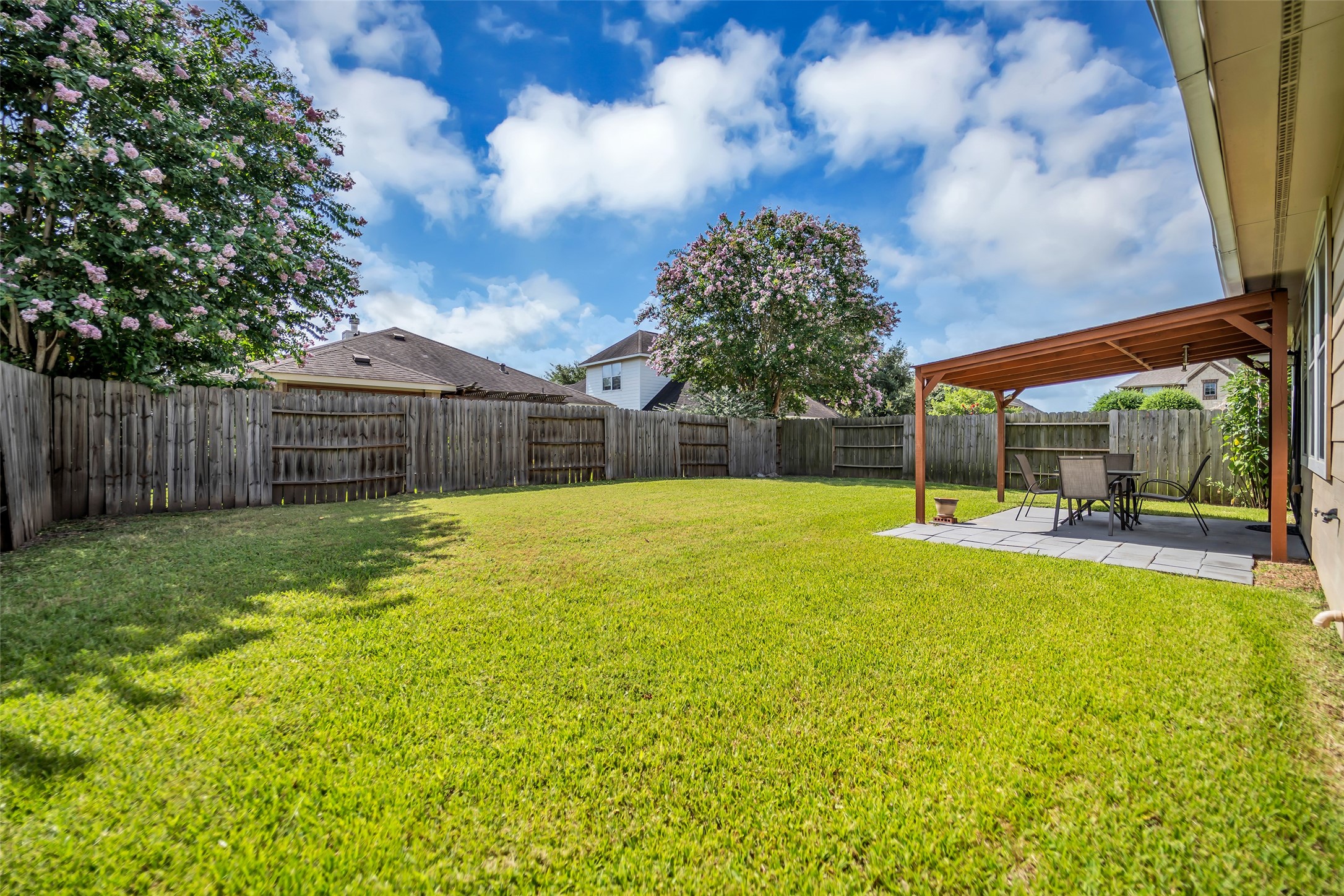 5406 Quarry Ridge Road Richmond, TX 77407 - Photo 36 of 36 View from the backyard highlighting the spacious, fully fenced lawn and covered patio designed for outdoor dining, relaxing, and year-round enjoyment. Mature crepe myrtles provide seasonal color while the generous yard offers plenty of space for entertaining, pets, play, or future outdoor additions.