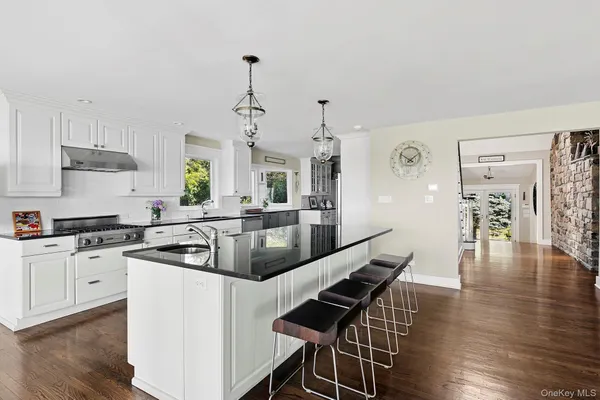 a kitchen with stainless steel appliances granite countertop a stove top oven a sink a refrigerator and white cabinets with wooden floor