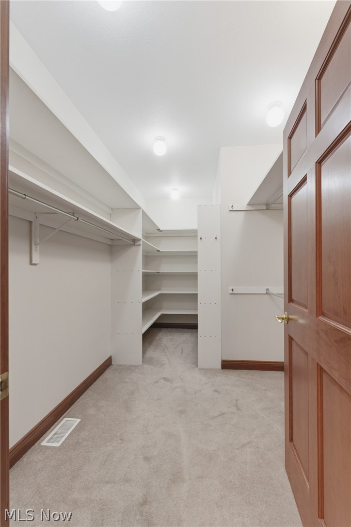 2184 Brenner Road Northeast Carrollton, OH 44615 - Photo 19 of 50 Walk-in closet featuring light gray carpet flooring, white built-in shelving, hanging rods, and a paneled wood door with brass hardware