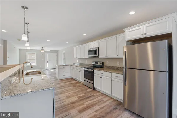 a kitchen with stainless steel appliances granite countertop a refrigerator a sink dishwasher a stove and white cabinets with wooden floor