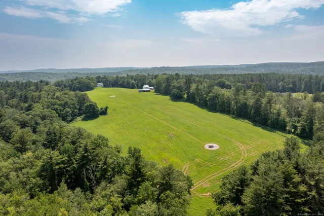 an aerial view of a residential houses with outdoor space and trees all around