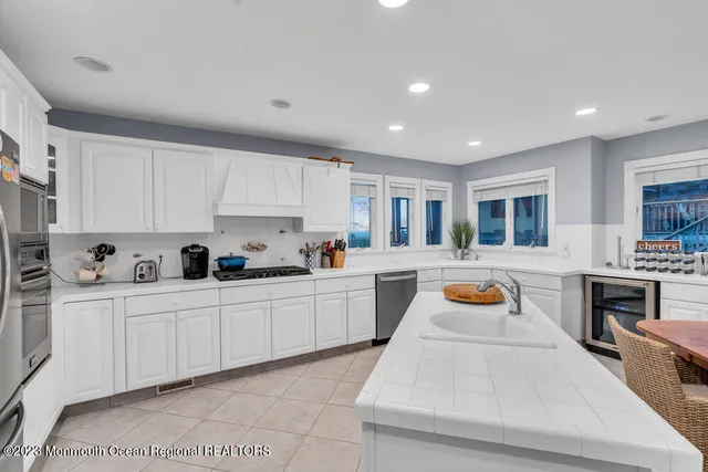 a large white kitchen with cabinets a sink a window and stainless steel appliances