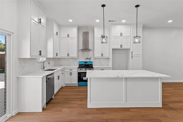 a kitchen with stainless steel appliances granite countertop a sink a stove a refrigerator and white cabinets