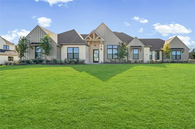 a view of a house next to a big yard with plants and large trees